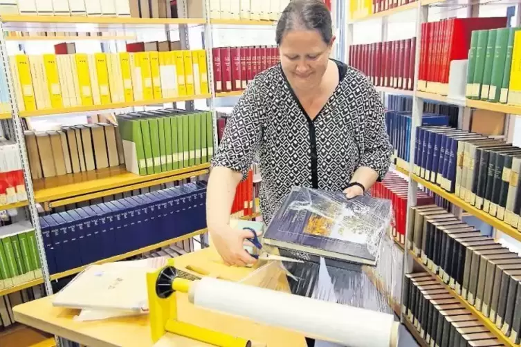 Landtagsarchiv-Mitarbeiterin Bettina Johnen rollt einen Bildband in Frischhaltefolie ein. Beutel und Folien gehören wie Overalls