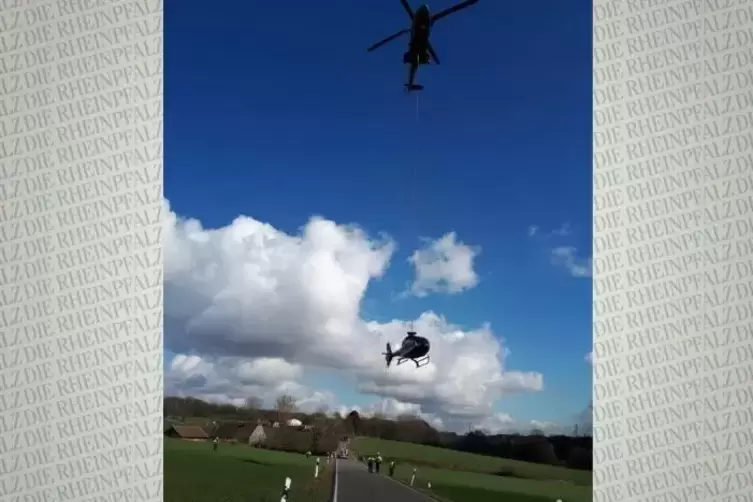 Ein Schulungshubschrauber der Bundespolizei hängt über einer Straße am Haken eines Lastenhubschraubers.