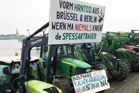 Traktoren mit Transparenten stehen vor Beginn einer Kundgebung von Bauern am Rheinufer. 