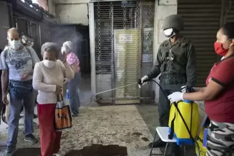 Kunden eines Supermarkts in der venezolanischen Hauptstadt Caracas werden von einem Soldaten mit einer desinfizierenden Lösung b