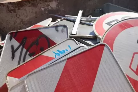 Beschmierte, verbogene und ausgebleichte Verkehrsschilder im Schrottcontainer einer Straßenmeisterei