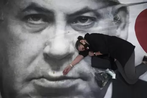 Nun kann er doch weiterregieren; Eine Demonstrantin in Tel Aviv, erschöpft auf einem Plakat von Premierminister Netanjahu. Er re