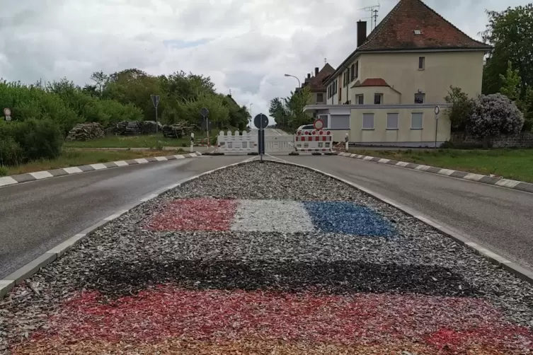 Die Tricolore und die Bundesflagge finden sich im Rindenmulch der Verkehrsinsel vor dem Grenz&uuml;bergang in Kr&ouml;ppen.