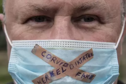 Ein Teilnehmer einer Kundgebung gegen die Corona-Maßnahmen der Regierung trägt einen Mundschutz mit der Aufschrift "Merkel-Dikta
