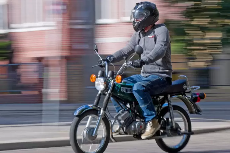 Ein Fahrlehrer fährt auf einem Simson S51 Moped durch die Stadt.