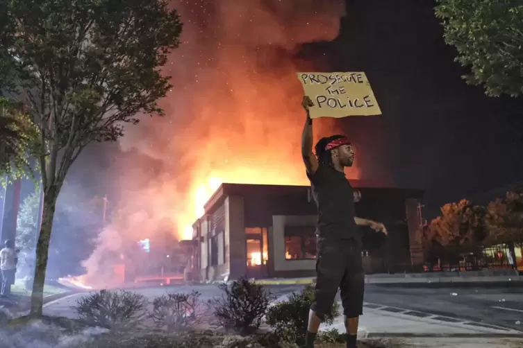 Atlanta: Ein Mann h&auml;lt ein Protest-Schild, w&auml;hrend im Hintergrund ein Wendy&rsquo;s-Restaurant brennt.