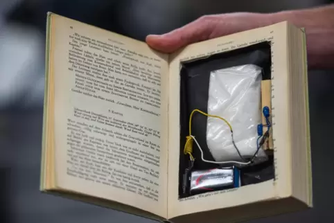Ein Polizeibeamter zeigt ein Buch das mit einer Zündvorrichtung und Sprengstoff manipuliert wurde. Im Kampf gegen gefährliche Ka