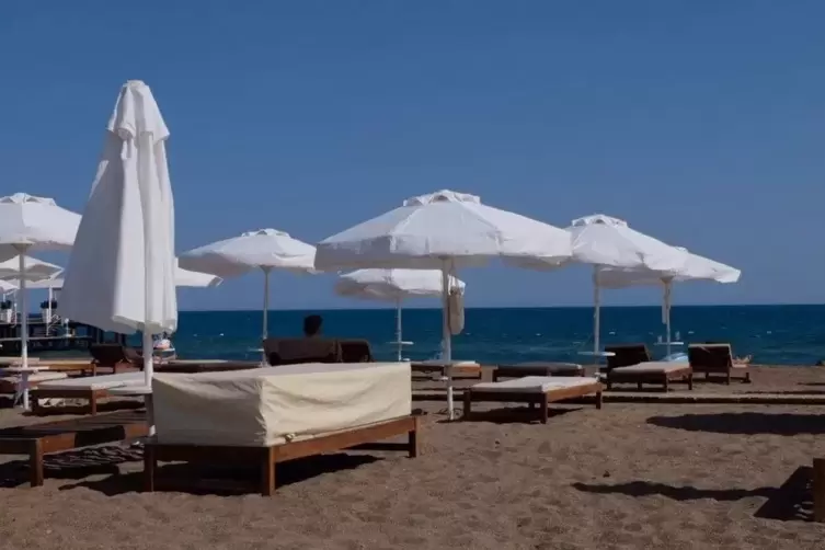 Strandliegen und Sonnenschirme stehen am menschenleeren Strand an einer Hotelanlage im türkischen Antalya.