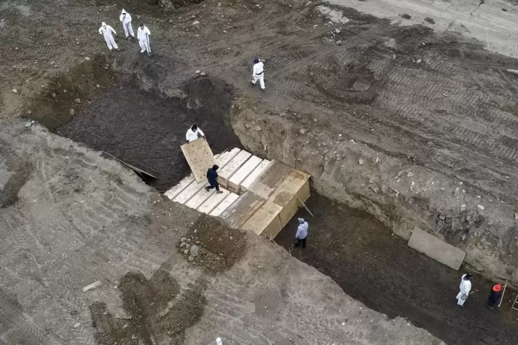 Arbeiter in Schutzanzügen vergraben einfache Holzsärge in einem Graben auf Hart Island, einer kleinen Insel, die New York vorgel