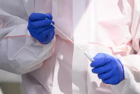 Ein Mitarbeiter hält in einem Abstrichzentrum einen Test auf das Coronavirus in Händen. 