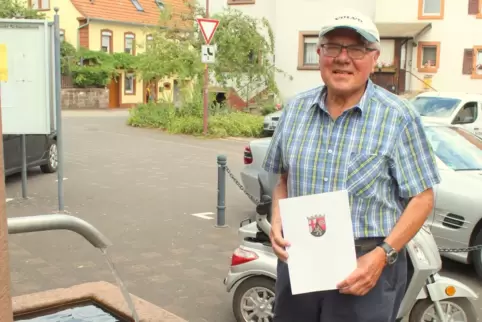 Fritz Schwarzmüller mit der Urkunde der Ministerpräsidentin am Dorfbrunnen in der Schwanheimer Ortsmitte.