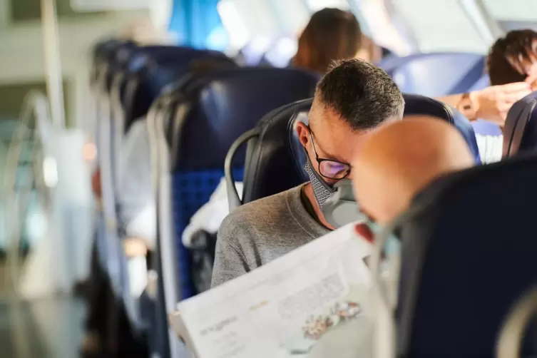 Reisende sitzen mit Nasen-Mund-Schutz in einem Zug.