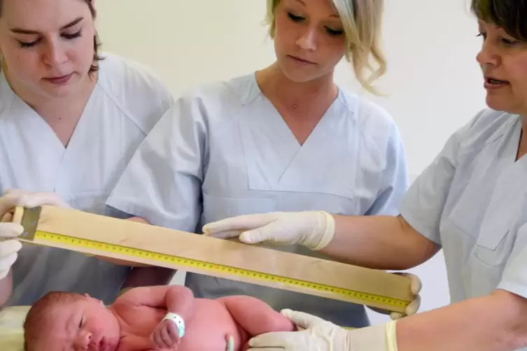Eine Leitende Hebamme zeigt Hebammenschülerinnen die Erstuntersuchung eines Neugeborenen.