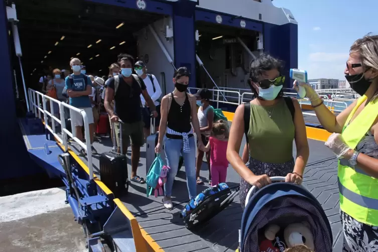 Griechenland, Piraeus: Eine medizinische Mitarbeiterin mit Schutzmaske misst die Körpertemperatur der Passagiere einer Fähre am 