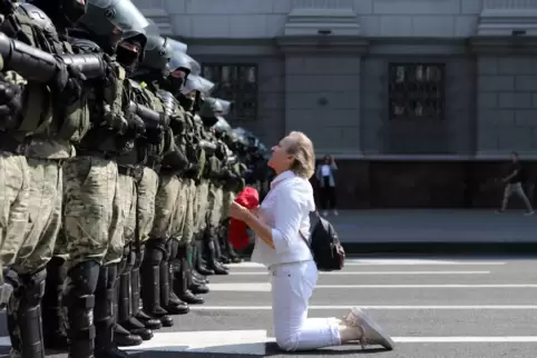  Eine Demonstrantin in Weiß redet kniend mit Polizisten. Viele ihrer Mitstreiterinnen haben noch Blumen dabei. 