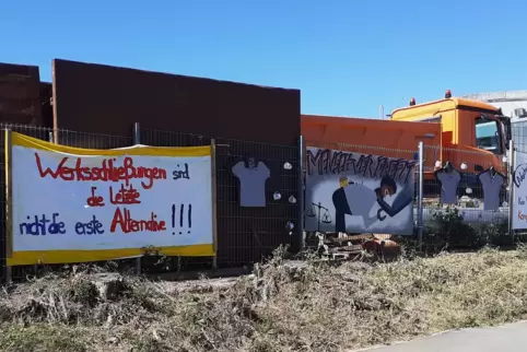 Beschäftigte haben Protestplakate gegen die Nordson-Schließung am Zaun gegenüber des Betriebes aufgehängt.