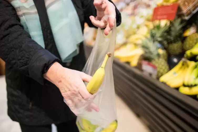 Eine Frau legt in einem Supermarkt eine lose Banane in eine Plastiktüte. 