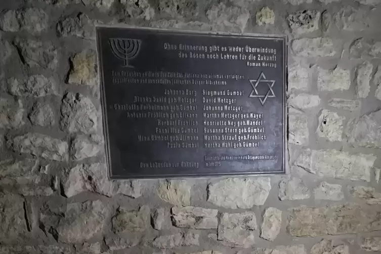 Eine Tafel erinnert im Gemeindepark in Albisheim an die jüdischen Opfer der NS-Diktatur. An der Mauer haben am Montagabend Mensc