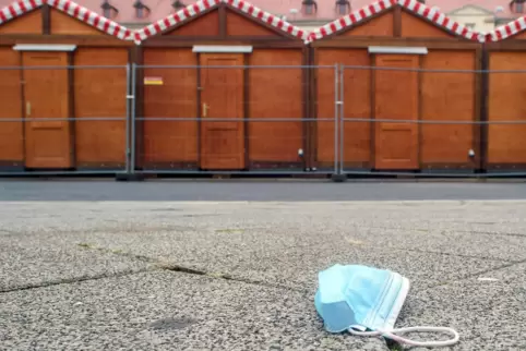 Ein Mund-Nasen-Schutz liegt vor geschlossenen Weihnachtsmarkt-Buden.