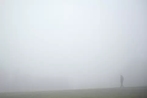 Ein Spaziergänger ist bei Nieselregen und Nebel auf einem Feldweg unterwegs. 