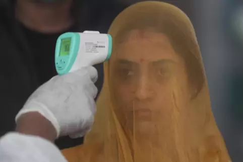 Ein Mitarbeiter des Gesundheitswesens prüft die Temperatur einer Passagierin am Bahnhof Bandra in Mumbai.