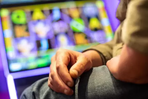 Ein Mann sitzt in einer Kneipe an einem Spielautomaten. 