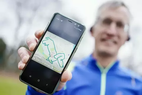 Norbert Asprion hält im Ebertpark sein Mobiltelefon mit dem Bild einer von ihm gelaufenen Wegstrecke in Form eines Hundes in der