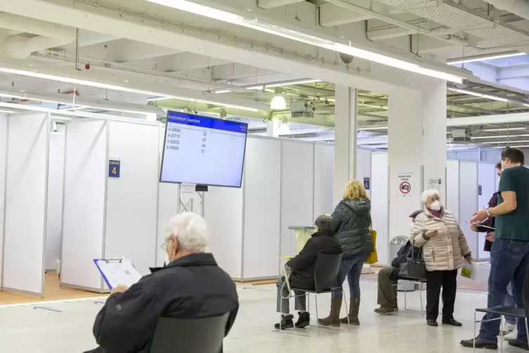 Wartebereich im Neunkircher Impfzentrum. Der Bildschirm zeigt an, welche Impfkabine jeweils zugewiesen wird.