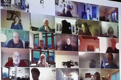 Die Stadtratsmitglieder klinken sich zuhause online in die Sitzung ein. Die Videokonferenz wird auf eine Leinwand in einem Raum Die Stadtratsmitglieder klinken sich zuhause online in die Sitzung ein. Die Videokonferenz wird auf eine Leinwand in einem Raum