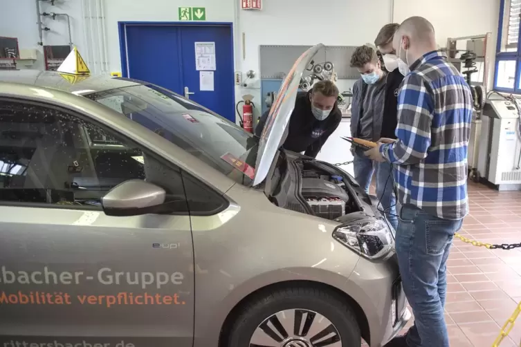 Die Auszubildenden Lucas Schann, Matteo Karl und Max Albrecht mit Werkstattleiter Stefan Plaul am neuen E-Auto. Die Schule hat l