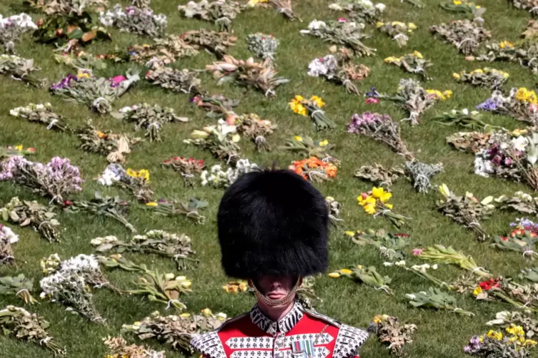 Eine königliche Wache steht auf dem Rasen von Schloss Windsor, der mit Blumensträußen übersät ist. 