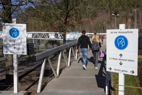 Schilder erinnern bei der Brücke auf der Gartenschau in Kaiserslautern an die Maskenpflicht. 