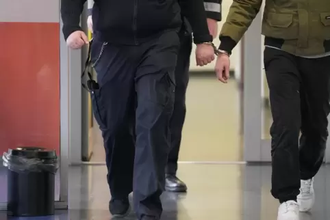 Ein Polizist führt einen jungen Mann in Handschellen zum Gerichtssaal. Damit viele Jugendliche in Ludwigshafen nicht so enden, a