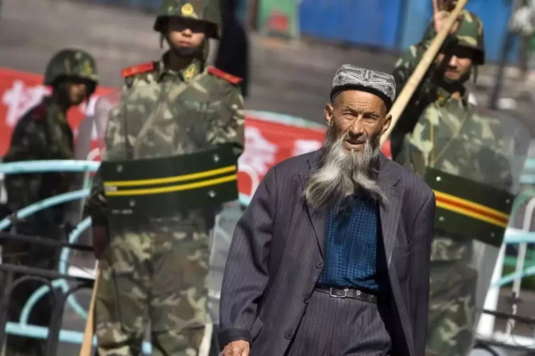 Ein Angehöriger der uigurischen Minderheit; im Hintergrund ein Mitglied der chinesischen Sicherheitskräfte in Xinjiang.