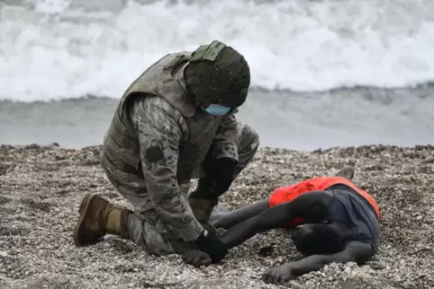Ein spanischer Soldat hilft einer Person, die am Strand von Ceuta liegt.