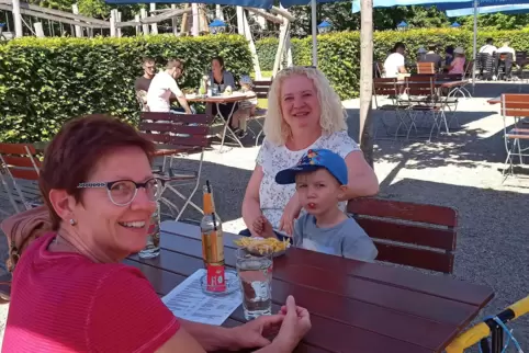 Susanne und Daven genießen den ersten Biergartenbesuch in diesem Jahr mit Pommes und Apfelschorle, links Ursula Kau-Michel, an e