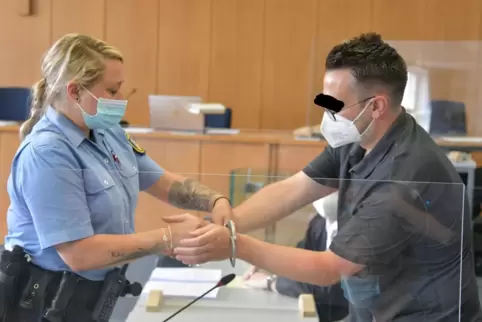 Eine Gerichtsbeamtin nimmt dem Angeklagten zu Prozessbeginn die Handschellen ab.