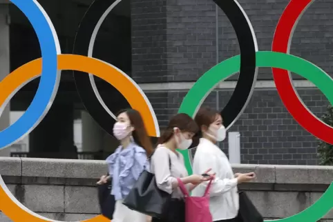 Menschen mit Gesichtsmasken gehen an der Statue der Olympischen Ringe in Tokio vorbei. 