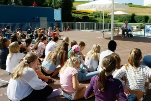 Fünftklässler des WEG lauschen dem Kinderbuchautor Will Gmehling im Freibad in Winnweiler.