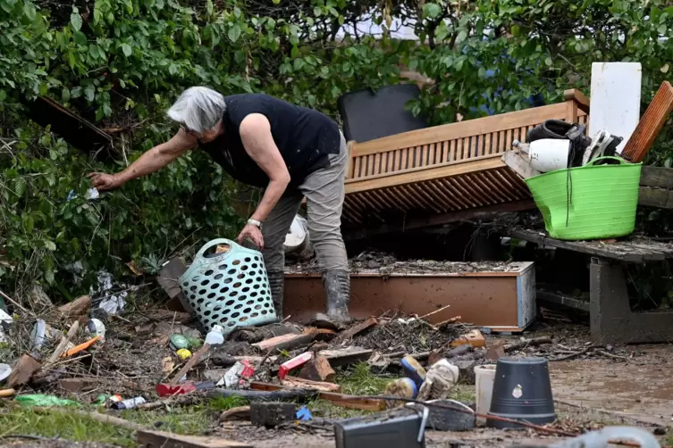Eine Frau sammelt nach dem Hochwasser in der rheinland-pfälzischen Ortsgemeinde Kordel Kleinteile aus einer Hecke.