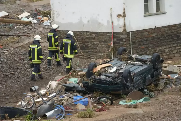 Feuerwehrleute gehen in der Gemeinde Schuld an einem zerstörten Auto vorbei. 