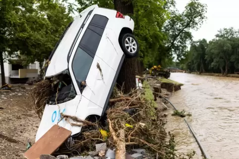 Ein vom Hochwasser angeschwemmtes Auto lehnt an einem Baum während im Hintergrund der Fluss Ahr zu sehen ist. Massive Regenfälle