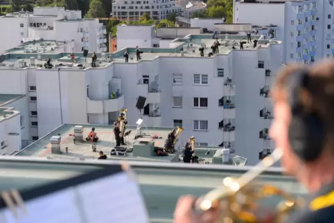 Ein Hornist spielt auf dem Dach eines Hamburger Hochhauses, während weitere Musiker auf den anderen Dächern stehen. 