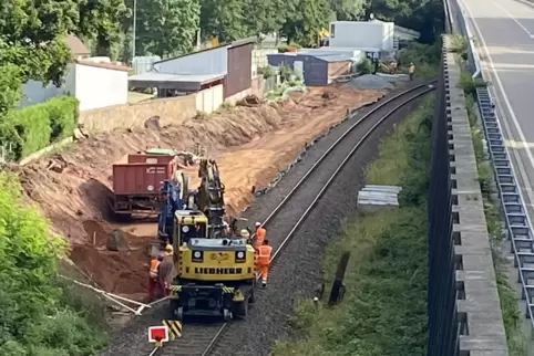 Einen auf den Schienen rollender Bagger trägt den Hang zur Landauer Straße hin ab, schafft Platz für den entstehenden Bahnsteig 