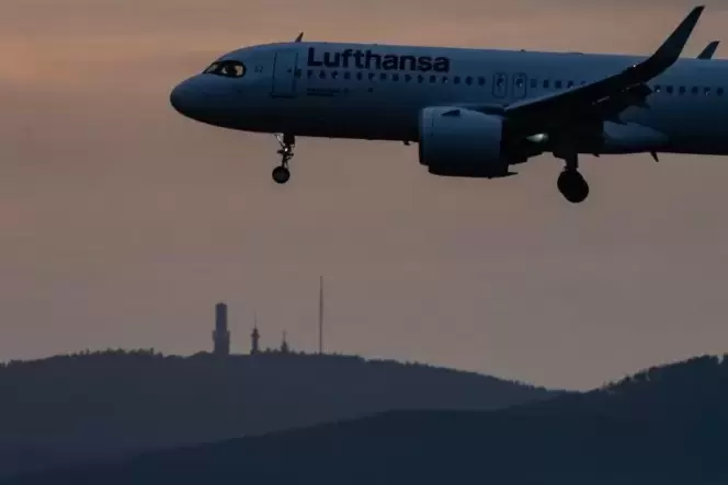 Eine Maschine der Lufthansa landet bei Einbruch der Dunkelheit auf dem Frankfurter Flughafen und fliegt dabei an der Kulisse de
