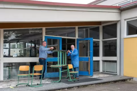 Gommersheims Ortschef Lothar Anton (links) und der langjährige Hausmeister Willi Keller vor der früheren Grundschule. Die Stühle