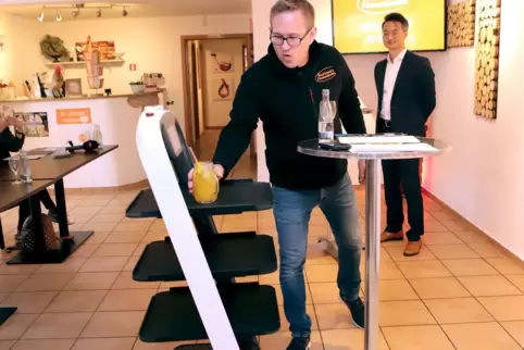 Christian Pudlo (links) nimmt ein Getränk von seinem Servierroboter entgegen, den die Firma von Sha He entwickelt hat. 