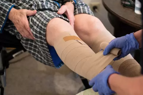 Eine ambulante Pflegerin bandagiert das Bein eines alten Mannes. 