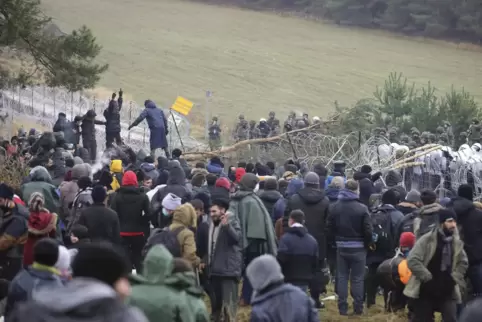Polnische Polizisten stehen hinter einem Stacheldrahtzaun, während sich an der belarussischen Grenze Migranten versammelt haben.