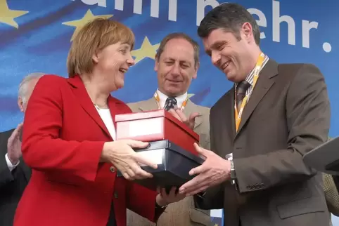 2004: Bernhard Matheis (rechts) beglückt Angela Merkel mit Pirmasenser Schuhen. Im Hintergrund steht Landtagsabgeordneter Erhard